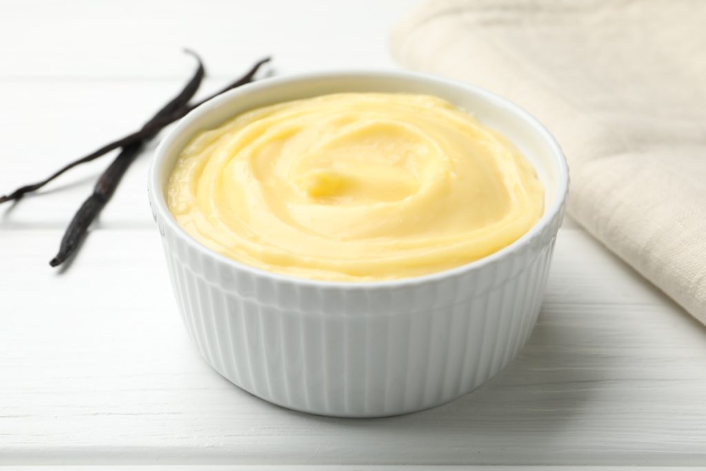 Un bol blanc rempli de crème pâtissière sur la table avec des vanilles