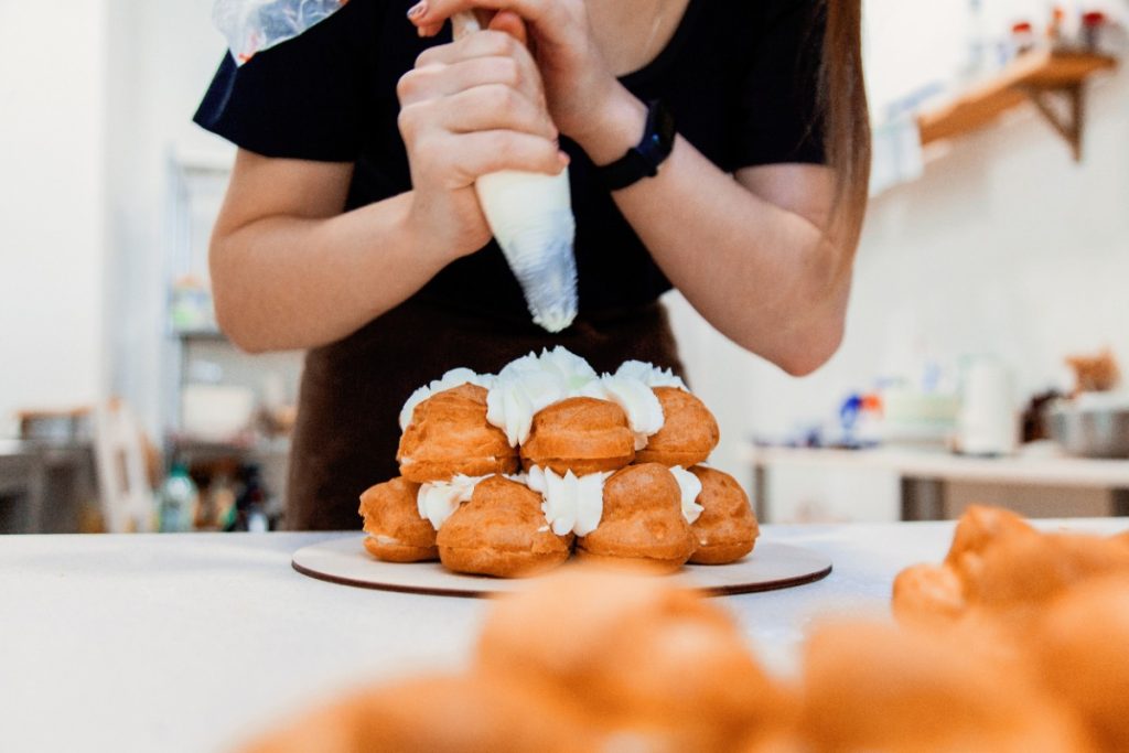Une boulangère décorant des choux avec de la crème