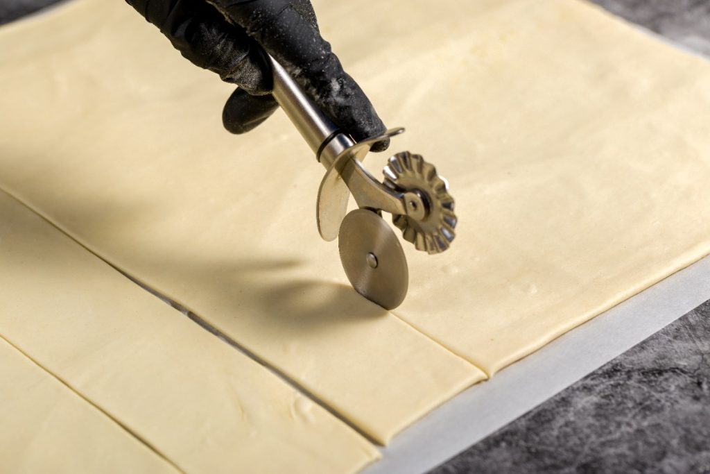 Un pâtissier coupant une pâte avec une roue cannelée