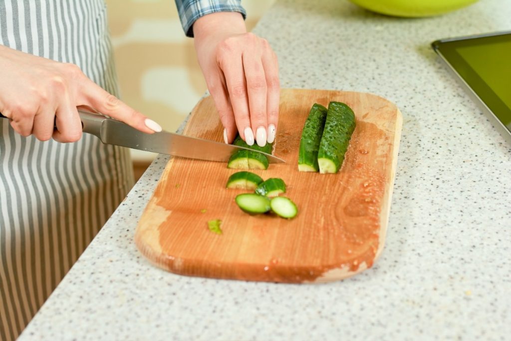 Une personne qui coupe une concombre sur une planchette en bois